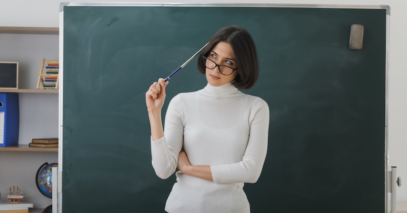 Pensive teacher standing in front of the desk