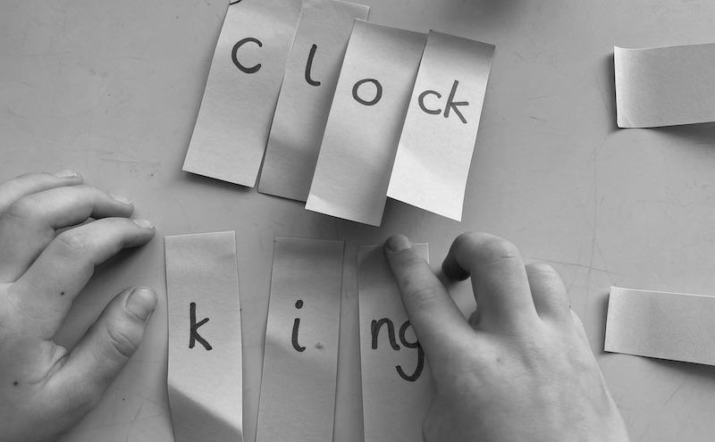 Narrow post it notes, each with a single grapheme, are attached to the table, forming words clock and king